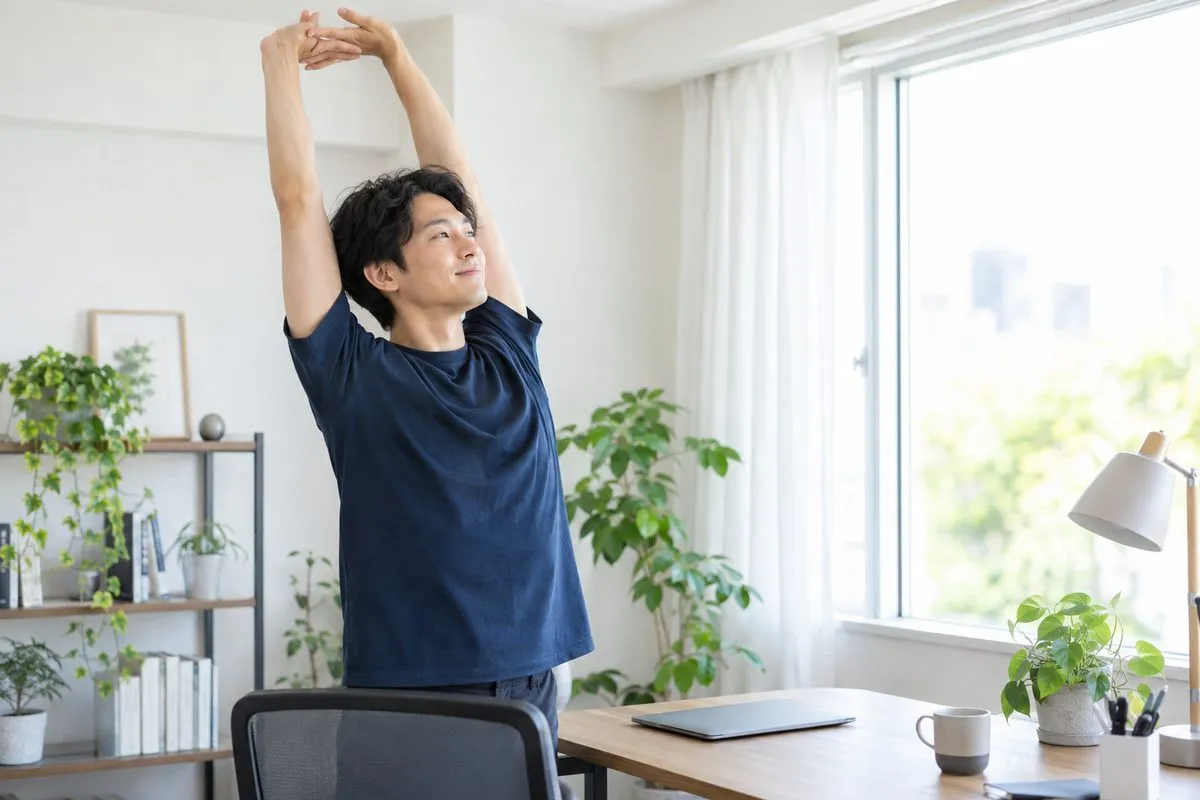 在宅勤務の合間にデスクの横で立ち上がり伸びをする男性
